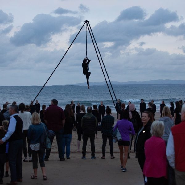 mapali, 2019 Ten Days' festival. A woman hangs high in the air over a crowd of onlookers watching a circus performance at dawn.