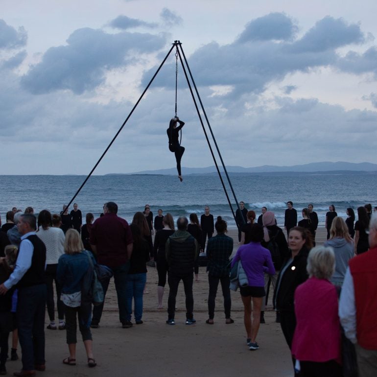 mapali, 2019 Ten Days' festival. A woman hangs high in the air over a crowd of onlookers watching a circus performance at dawn.