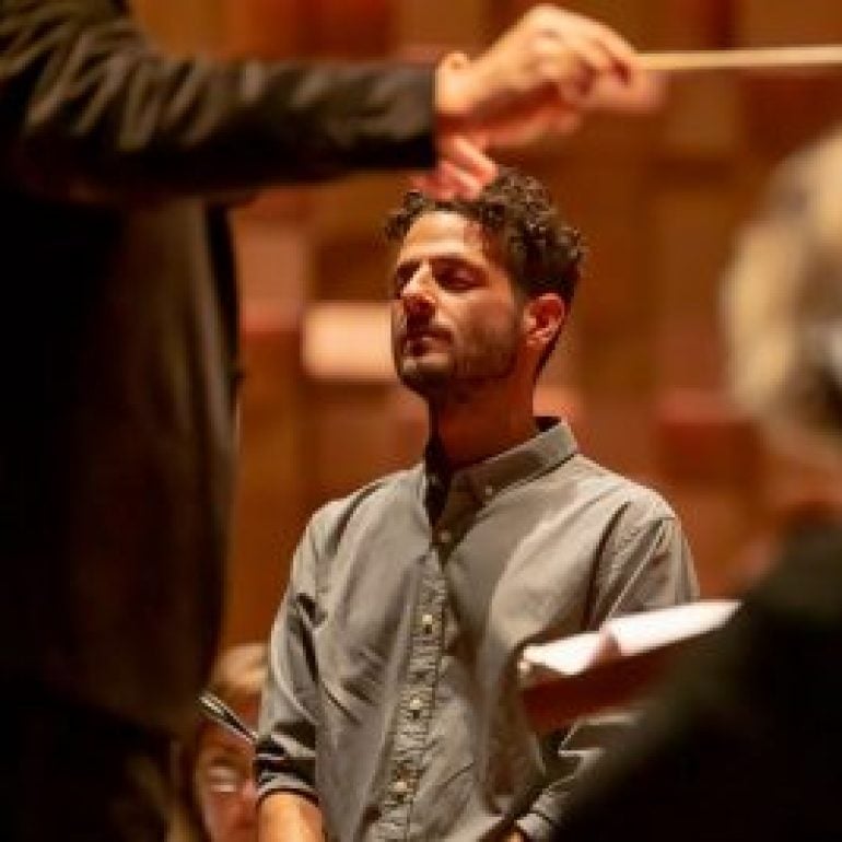 An image of a man with his eyes closed in front of a conductor, he is a member of the performance