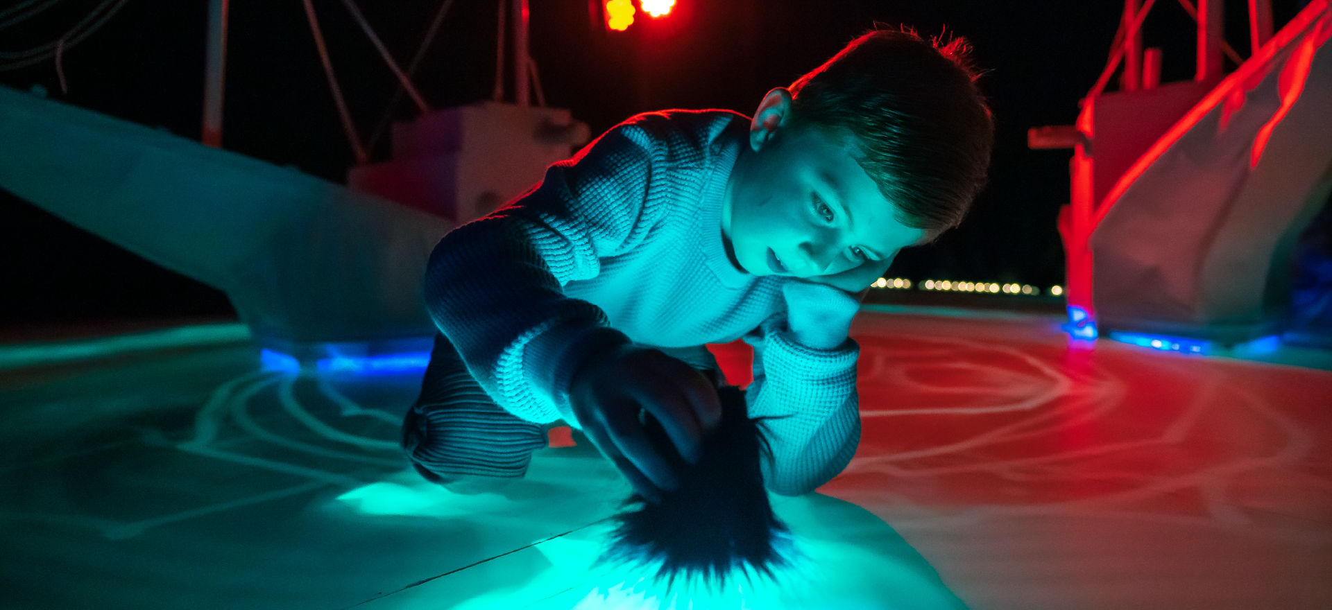 Sea of Light hero image, boy looking at ground holding a black fluffy toy, the light beneatht he toy is bright light blue