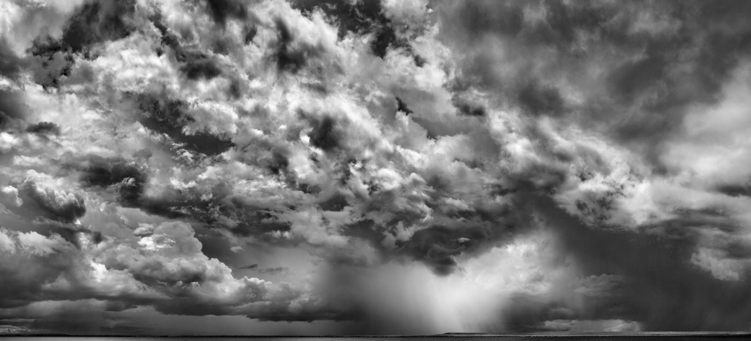 A black and white picture of a dark and cloudy sky above a calm body of water.