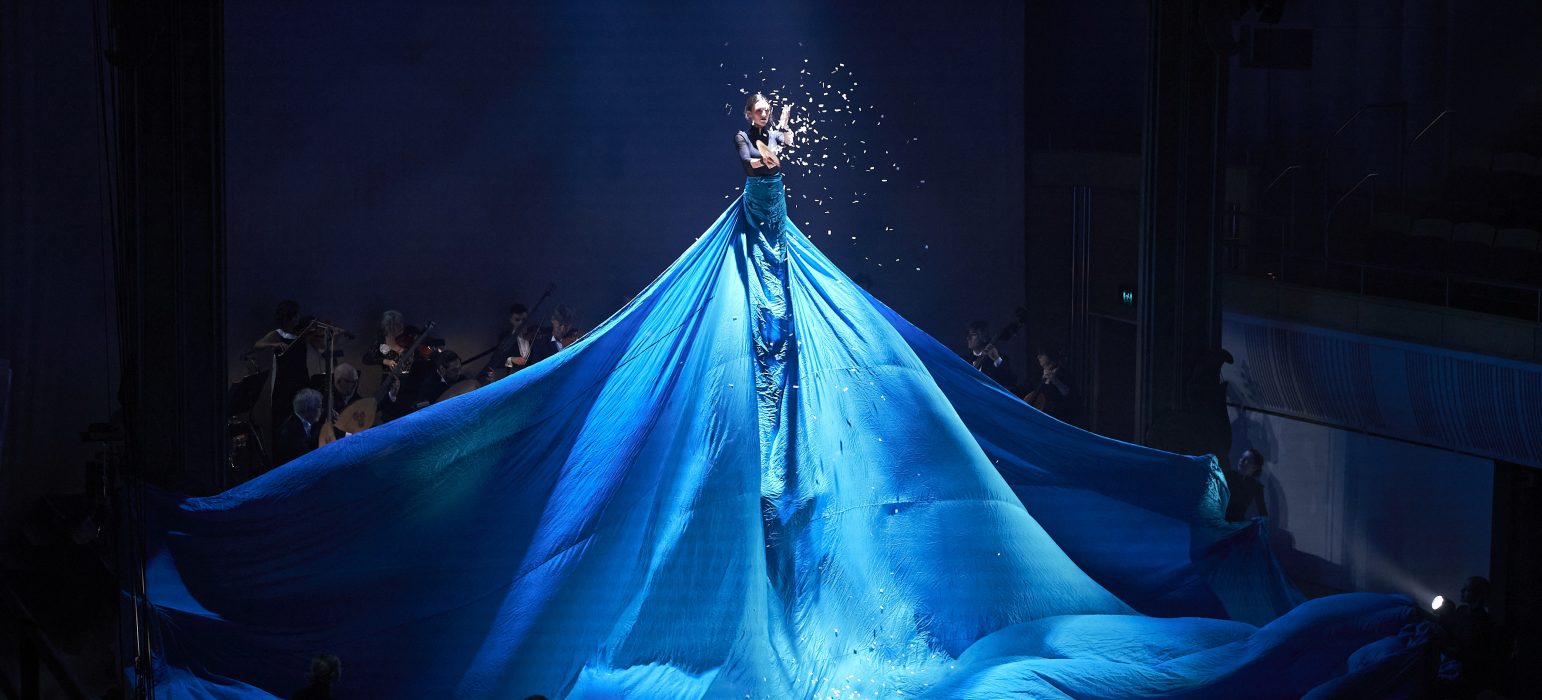 A person in a blue gown is under stage lighting