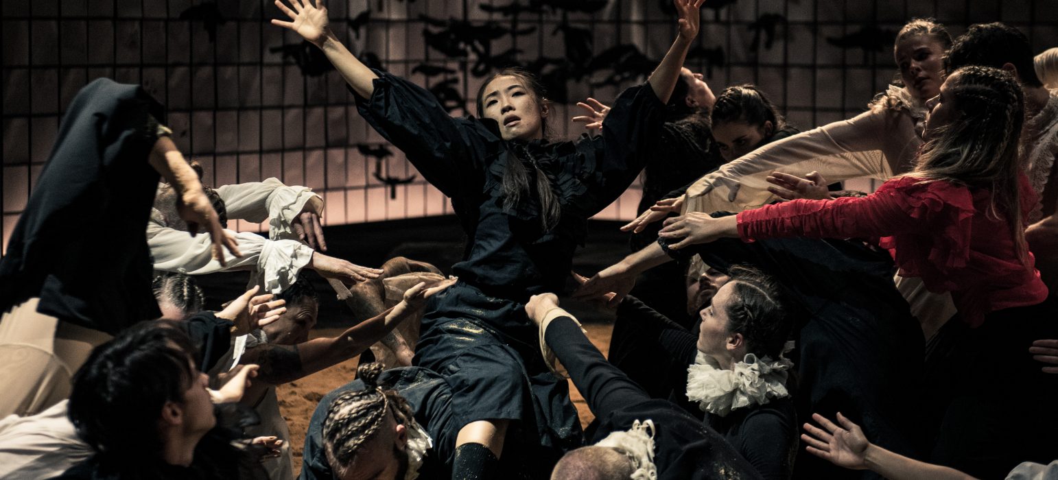 Archives of Humanity hero image, a person is surrounded by people all moving closer to her, she has her arms up in the air and looks to be singing