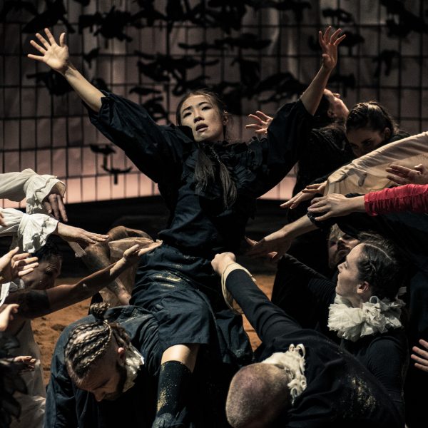 Archives of Humanity hero image, a person is surrounded by people all moving closer to her, she has her arms up in the air and looks to be singing
